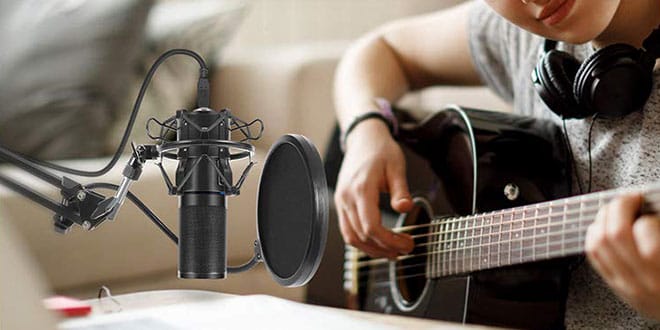 A person playing an acoustic guitar in front of a microphone.
