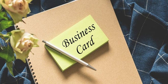 A business card on a notebook with roses and a pen.
