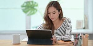 A woman is sitting at a table and using a tablet.