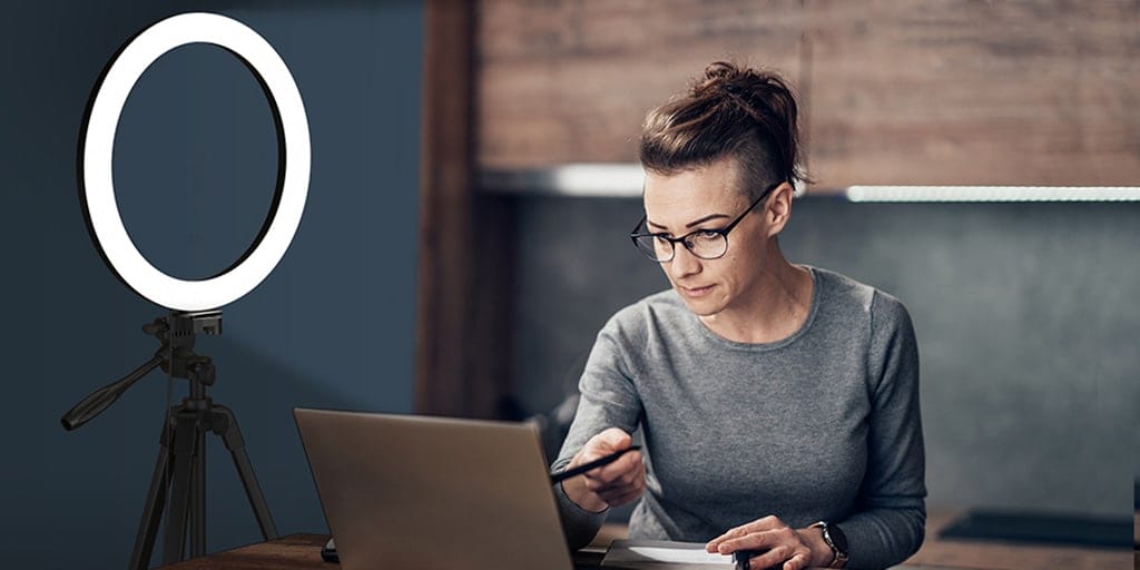 A woman using a laptop and a ring light.