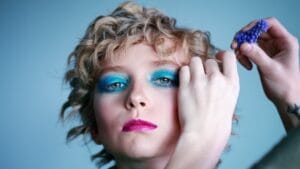 A woman wearing teal eyelashes is getting her makeup done by a makeup artist.