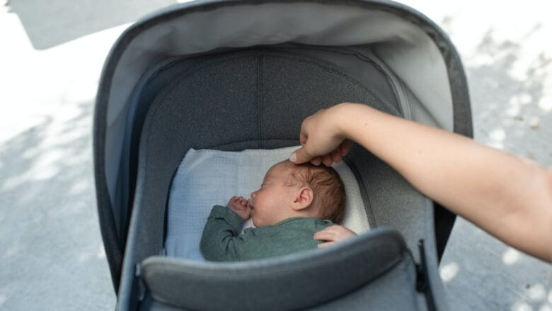 A cute baby sleeping in a gray stroller.