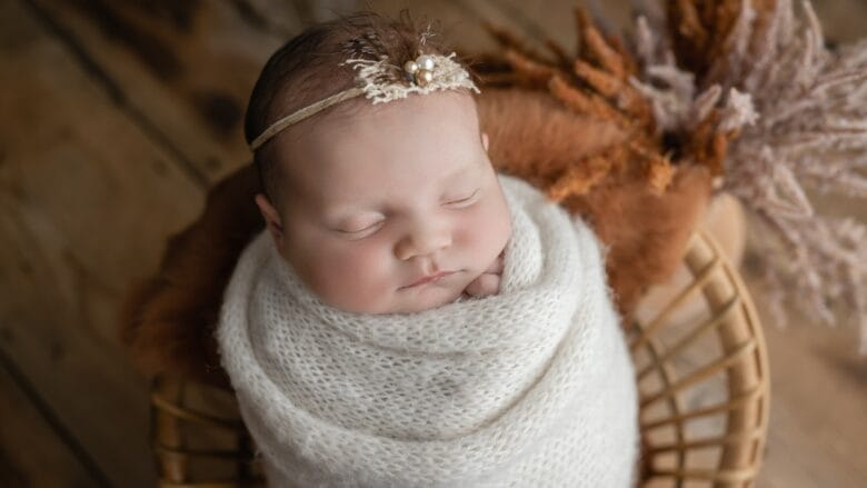 A baby girl is wrapped in a blanket and sleeping in a basket.