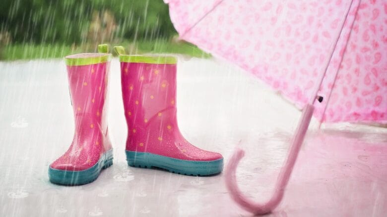 A pair of pink rain boots and an umbrella in the rain.