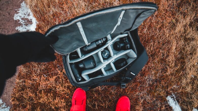 A person standing in the snow holding a camera bag.