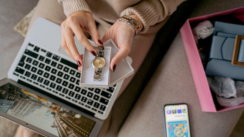 A woman using a laptop and holding a box with wrist watch.