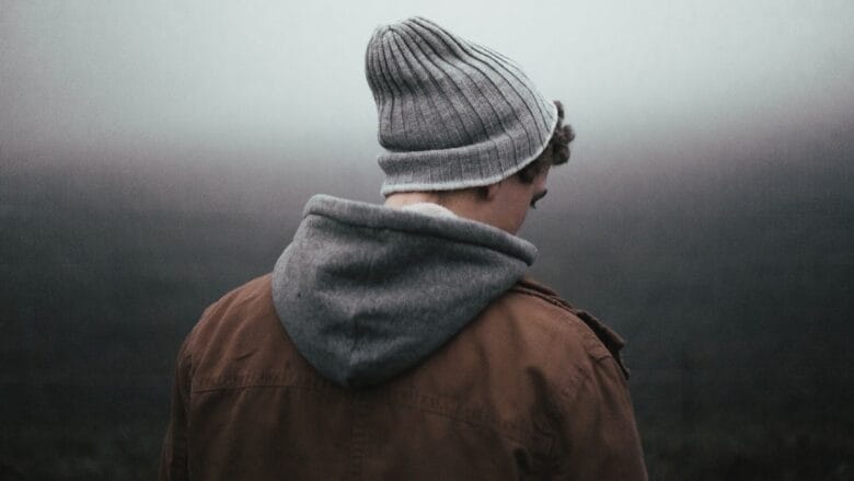 A man wearing a beanie is standing in a field on a foggy day.