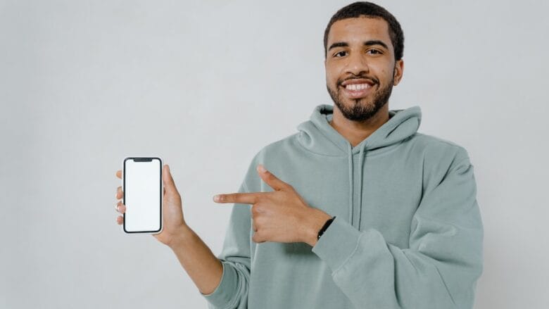 A man in gray hoodie pointing his finger at a blank screen on a gray background.
